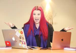 Excalibur Press trainer Tina Calder looking excited with 2 laptops in front of her and her arms stretched out to advertise the webinar How To Set Up Your Social Media Content Strategy & Plan For 2022