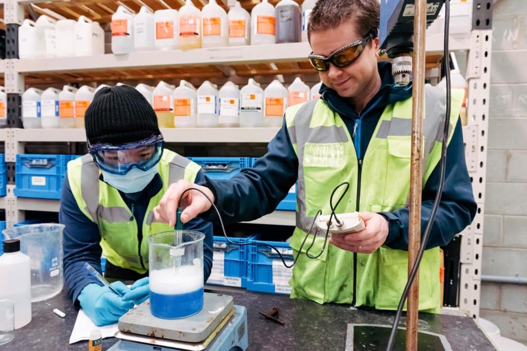 Dr Adam Hunniford founder of PiP Chemicals in Newtownards standing in the warehouse beside a shelf full of chemicals containers, Dr Hunniford is wearing a high vis vest