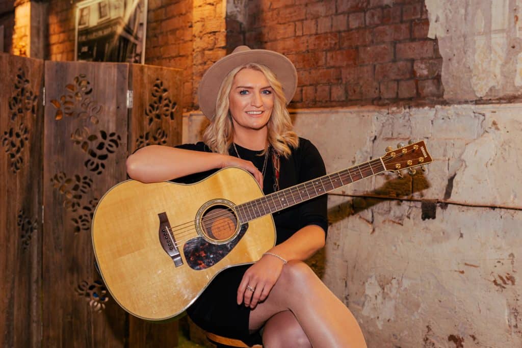 Singer songwriter Amanda St John sitting on stool with guitar at St Joseph's Church in Sailortown Belfast